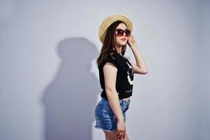 ritratto di una ragazza attraente in maglietta nera che dice lol, pantaloncini di jeans, cappello e occhiali da sole in posa in studio. foto