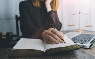 concetto di giustizia e diritto. giudice maschio in un'aula di tribunale con il martelletto, lavorando con computer e tastiera docking, occhiali, sul tavolo alla luce del mattino foto