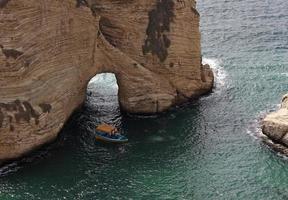 una piccola barca passa un grande scoglio sulla costa di Beirut, in Libano foto