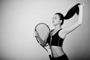 ritratto in bianco e nero di bella giovane donna giocatore in abiti sportivi che tiene la racchetta da tennis mentre in piedi su sfondo bianco. foto