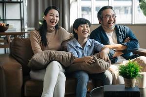 felice famiglia asiatica che trascorre del tempo guardando la tv insieme sul divano in soggiorno. concetto di famiglia e casa foto