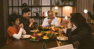 la grande famiglia asiatica chiude gli occhi e prega le mani quando dice la grazia pregando prima di cenare a casa foto