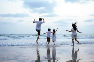 famiglia asiatica che corre e salta insieme alla spiaggia con il concetto felice della spiaggia di viaggio di vacanza dei bambini foto