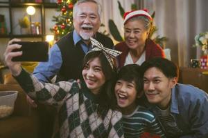 famiglia asiatica che prende selfie vicino all'albero di natale insieme a casa. famiglia, vacanze, concetto di natale foto