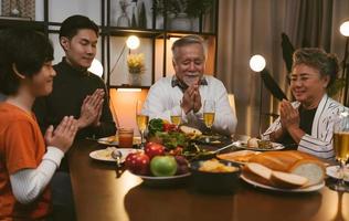 la grande famiglia asiatica chiude gli occhi e prega le mani quando dice la grazia pregando prima di cenare a casa foto