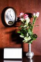 orologio da parete, calendario vuoto e rose rosa in brocca foto