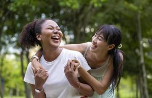 la diversità della coppia lesbica lgbtq ride e si abbraccia mentre si gode il tempo libero all'aperto nel parco pubblico durante l'estate foto