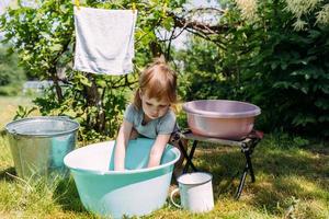 la bambina in età prescolare aiuta con il bucato. il bambino lava i vestiti in giardino foto