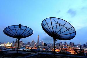 antenna parabolica nera di comunicazione sopra il cielo al tramonto nel paesaggio urbano foto