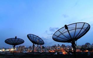 antenna parabolica nera di comunicazione sopra il cielo al tramonto nel paesaggio urbano foto