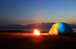 tenda e falò al tramonto, in riva al lago foto