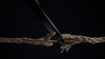 la corda tesa viene tagliata con un coltello su uno sfondo scuro. la corda sta per spezzarsi. il concetto di pericolo di rottura. foto