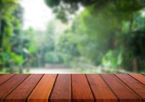 messa a fuoco selezionata tavolo in legno marrone vuoto e giardino verde o foresta sfocano lo sfondo con immagine bokeh. per il tuo fotomontaggio o la visualizzazione del prodotto. foto