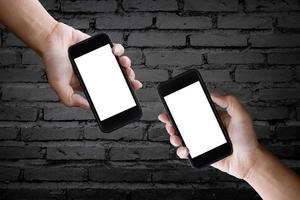 due mani che tengono lo schermo vuoto di uno smartphone sul vecchio muro di mattoni neri. foto