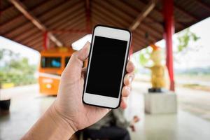 mano sinistra che tiene utilizzando lo smartphone con schermo vuoto su sfondo sfocato astratto della stazione ferroviaria. foto