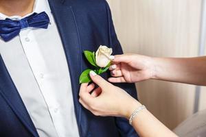 la sposa mette lo sposo su un fiore all'occhiello di rose bianche il giorno del matrimonio foto