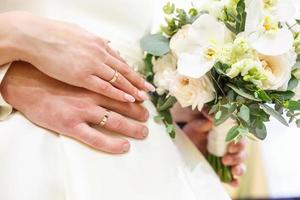 lo sposo abbraccia la sposa con il bouquet di rose bianche da sposa. anelli sulle mani di sposi novelli foto
