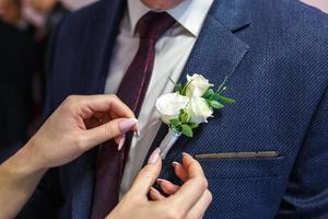 la sposa mette lo sposo su un fiore all'occhiello di rosa e rosa bianca il giorno del matrimonio foto