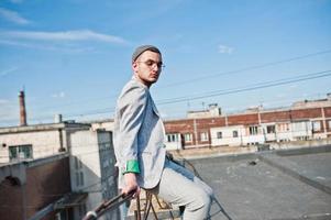 sognatore elegante uomo macho in abito grigio, cappello e occhiali in posa sul tetto. foto