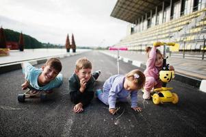 quattro ragazzini in asfalto giocano e si divertono. la famiglia sportiva trascorre il tempo libero all'aria aperta con scooter e pattini. foto