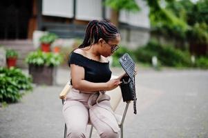 elegante donna afroamericana in occhiali da sole poste all'aperto sulla sedia. foto