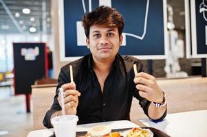 elegante uomo indiano seduto al fast food cafe e mangiare patatine fritte. foto