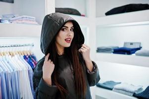 bruna splendida ragazza nella boutique del negozio di abbigliamento in giacca invernale con felpa con cappuccio. foto