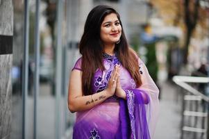 ragazza indù indiana al tradizionale saree viola posato in strada e mostra il segno delle mani tatuate di namaste. foto