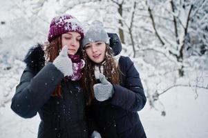 due amiche divertenti che si divertono in una giornata nevosa invernale vicino ad alberi innevati. foto