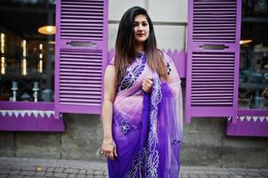 ragazza indù indiana al tradizionale saree viola poste in strada contro le finestre viola. foto