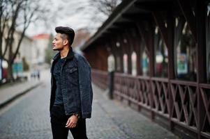 uomo indiano bello e alla moda in giacca di jeans nera posata all'aperto. foto