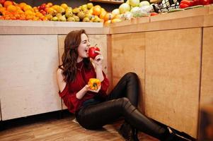 ragazza in rosso che tiene due peperoni sul negozio di frutta. foto