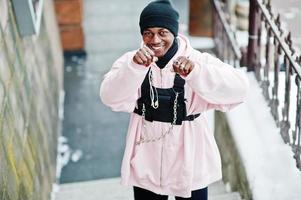 elegante uomo afroamericano in stile urbano con felpa con cappuccio rosa in posa al giorno d'inverno e mani di boxe. foto