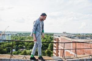 sognatore elegante uomo macho in abito grigio, cappello e occhiali in posa sul tetto. foto