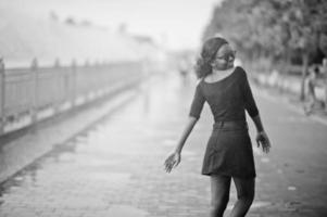 ragazza afroamericana in occhiali da sole, vestiti neri e camicia in posa all'aperto. donna di colore alla moda contro la pioggia di fontane. foto