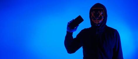 hacker anonimo e maschera facciale con smartphone in mano. foto