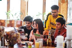 gruppo di amici asiatici seduti al caffè. felici indiani che si divertono insieme, seduti sul divano e scelgono i pasti dal menu. foto