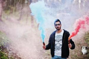 l'uomo arabo di street style con gli occhiali tiene il bagliore della mano con una bomba fumogena rossa e blu. foto