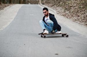 uomo arabo in stile street con occhiali da vista con longboard longboard lungo la strada. foto