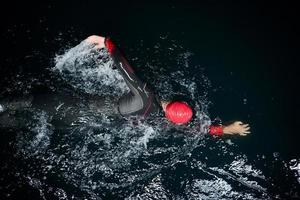 atleta di triathlon che nuota nella notte buia che indossa la muta foto