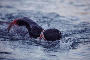 atleta di triathlon che nuota sul lago all'alba indossando la muta foto