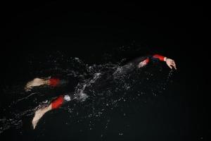 atleta di triathlon che nuota nella notte buia che indossa la muta foto