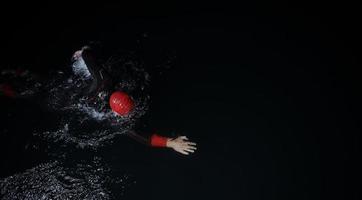 atleta di triathlon che nuota nella notte buia che indossa la muta foto