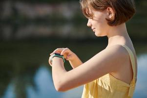 un'adolescente allestisce un fitness tracker sullo sfondo del lago. passeggiata. foto