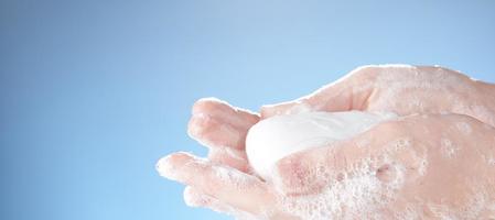 sapone bianco nelle mani saponose delle donne su sfondo blu. foto dallo spazio di copia.