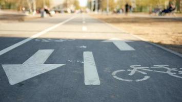 simbolo della bicicletta sulla strada della città sullo sfondo del parco e persone che camminano sfocate. foto