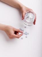 mani femminili che tengono le pillole e il bicchiere d'acqua della medicina foto