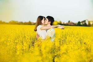 le giovani coppie innamorate si abbracciano e si baciano appassionatamente mentre posano contro un campo di fiori giallo, dimostrano relazioni sincere e devozione. concetto di persone, amore e devozione foto