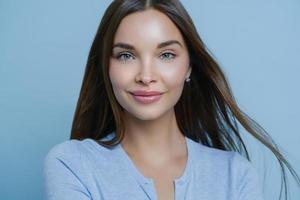 l'inquadratura orizzontale di una giovane donna con capelli lisci scuri, aspetto fresco e trucco, si prende cura della sua pelle soddisfatta del prodotto per la cura della pelle lascia un commento positivo pone in studio indoor. bellezza, cosmetologia foto