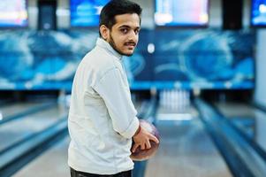 uomo del sud asiatico in camicia di jeans in piedi alla pista da bowling con la palla sulle mani. ragazzo si sta preparando per un tiro. foto